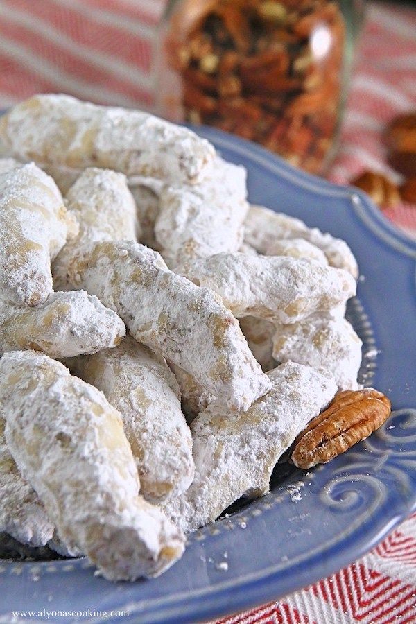 a blue plate topped with powdered sugar cookies and pecans next to a jar of nuts