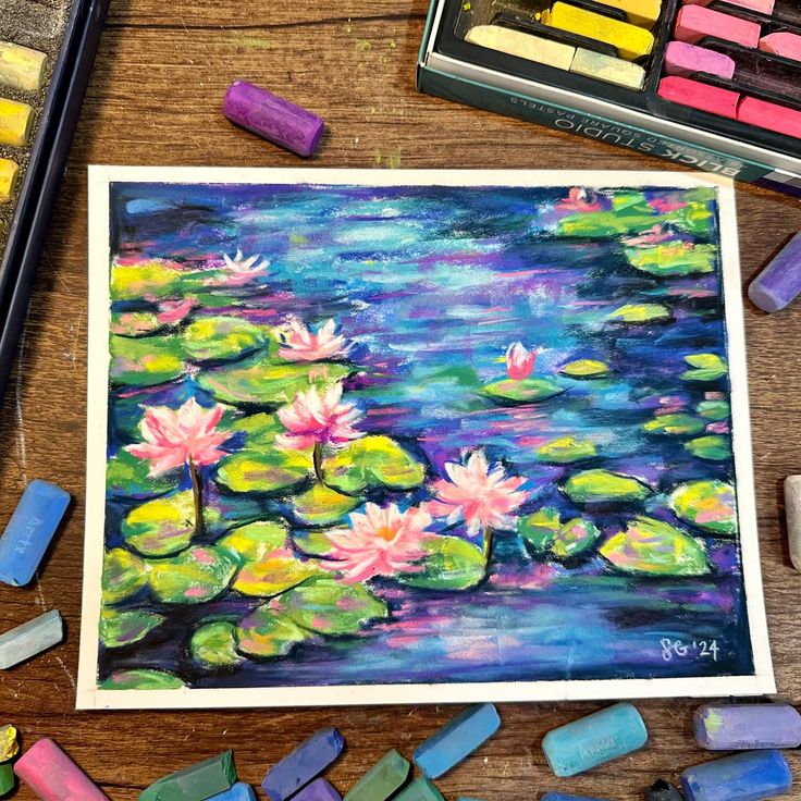 some crayons are laying next to a painting with water lilies