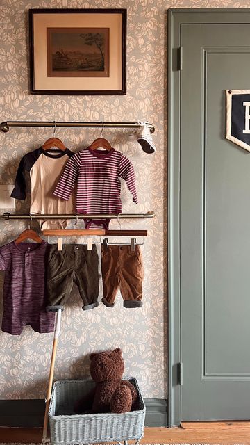 a teddy bear is sitting in front of a wall with clothes hanging on the rack