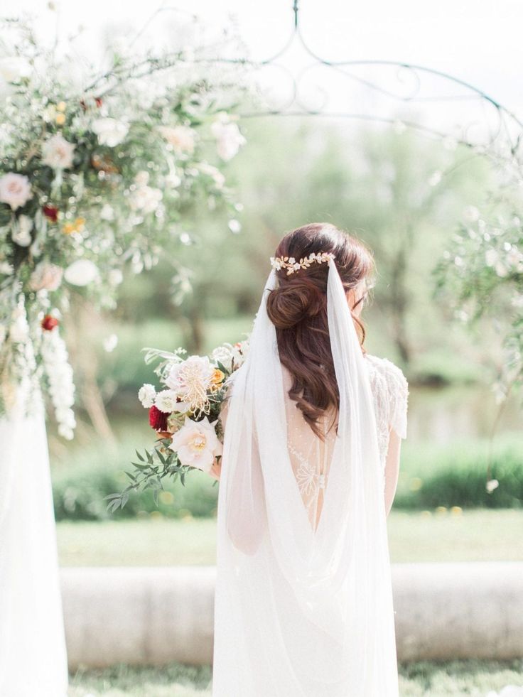 a woman in a wedding dress standing under an arch with flowers