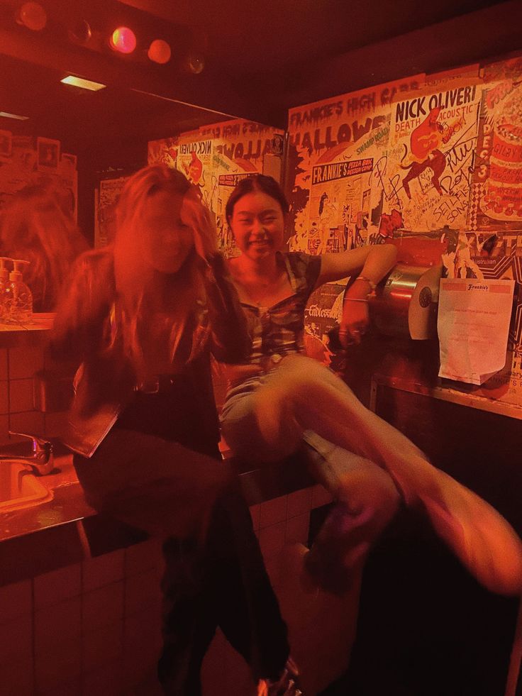 two women sitting at a counter in a bar with posters on the wall behind them