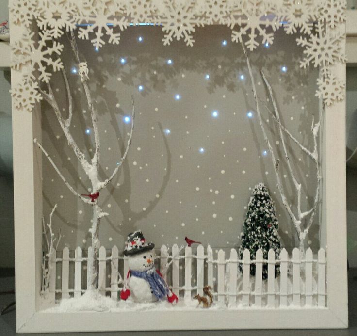 a snowman sitting in front of a white picket fence with trees and lights behind it