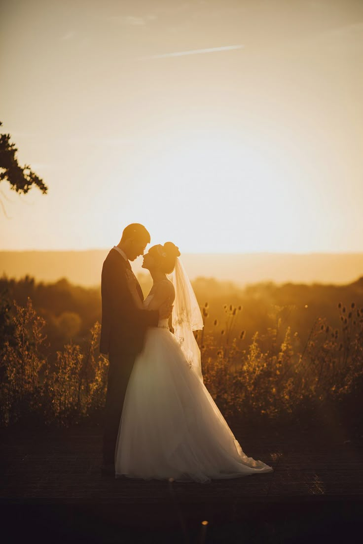 a bride and groom kissing in front of the setting sun at their wedding ceremony on top of a hill