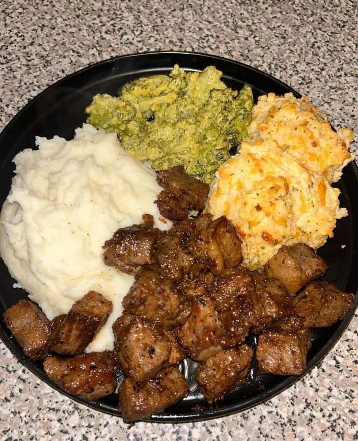 a black plate topped with meat, mashed potatoes and broccoli