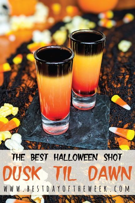 two glasses filled with orange and black liquid on top of a table covered in candy corn