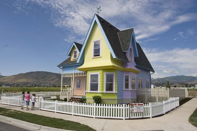 two people standing in front of a colorful house with white picket fence and green grass