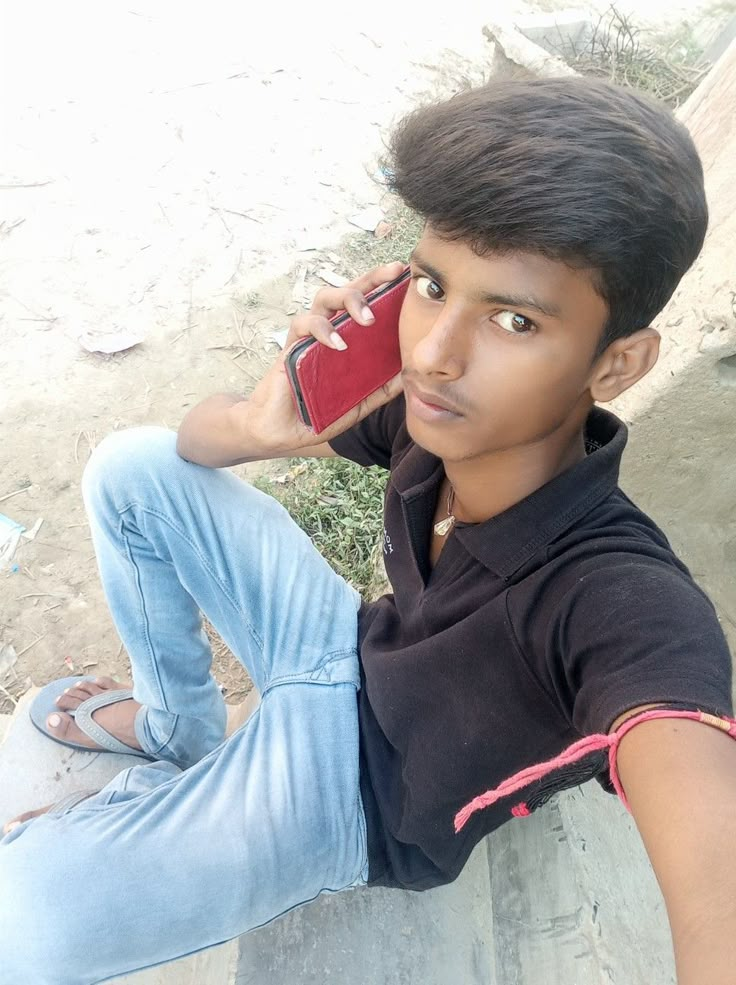 a young man sitting on the ground talking on a cell phone with his hand up to his ear