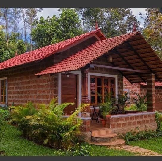 a small brick house in the middle of some trees and grass with plants around it