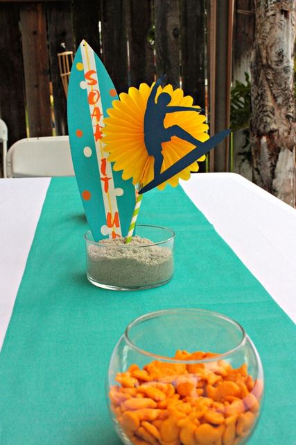 a table topped with a bowl of candy and a surfboard decoration on top of it