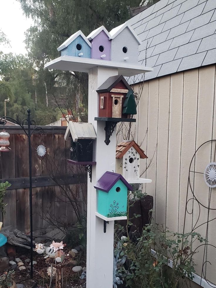 several bird houses are attached to the side of a house on a pole in front of a fence