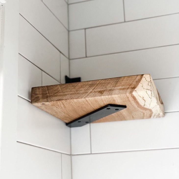 a wooden shelf mounted to the side of a white tiled bathroom wall next to a window