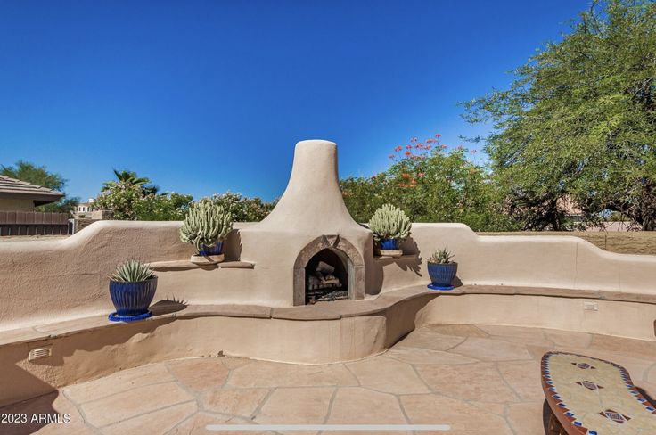 an outdoor fireplace in the middle of a patio with potted cacti on it