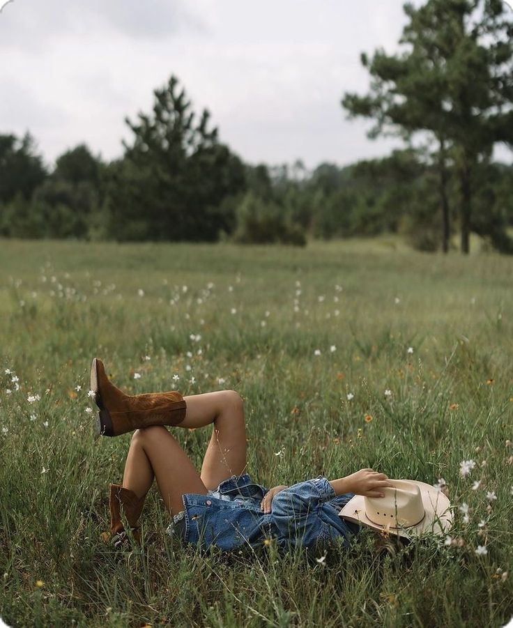 a woman laying on the ground in a field with her legs crossed and wearing cowboy boots