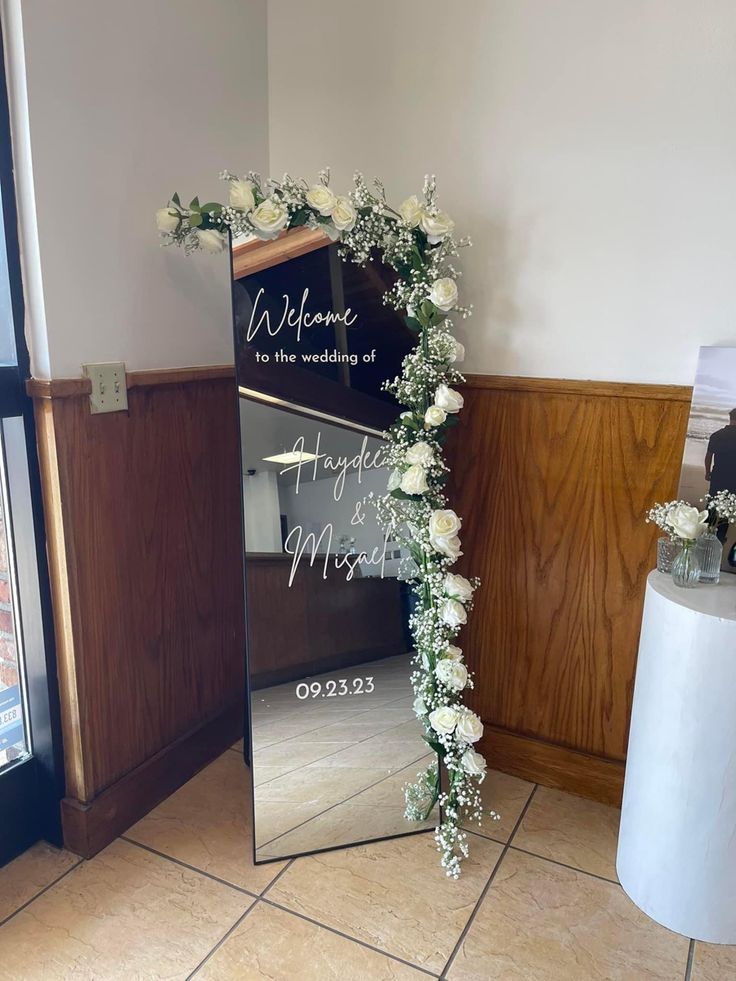 a mirror with flowers on it sitting in front of a sign that says welcome to the bride and groom