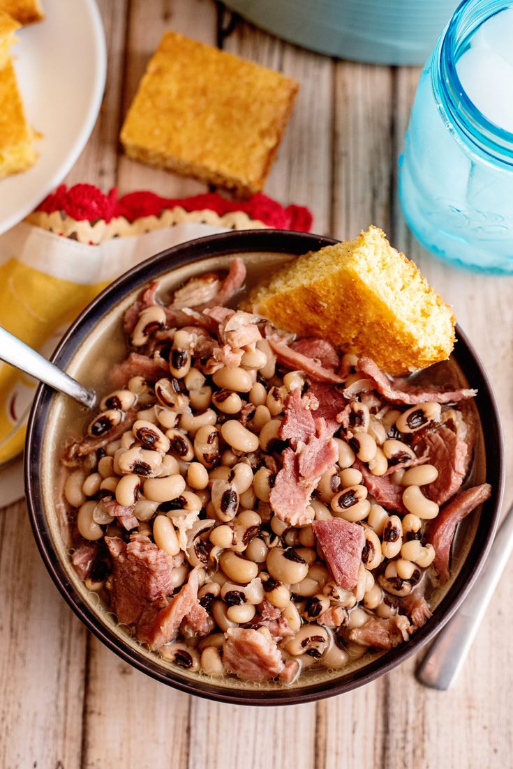 a bowl filled with beans and ham next to cornbreads on a wooden table