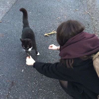 a woman kneeling down petting a black and white cat on the street next to a banana peel