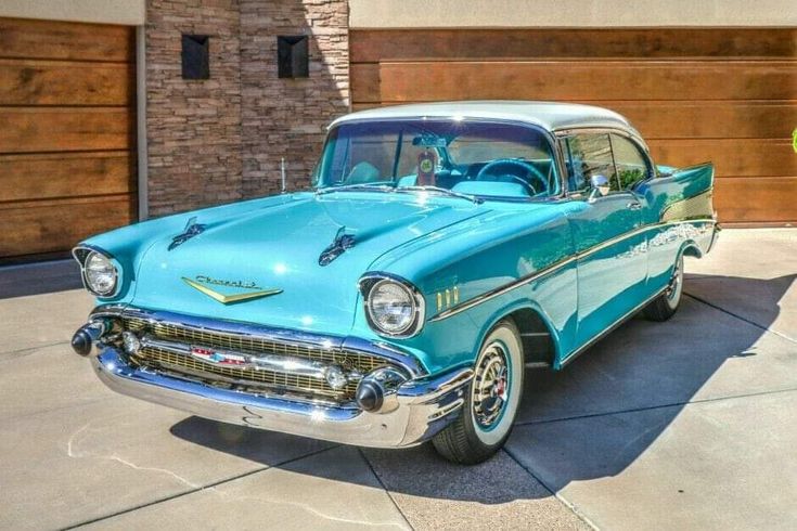 an old blue car parked in front of a garage