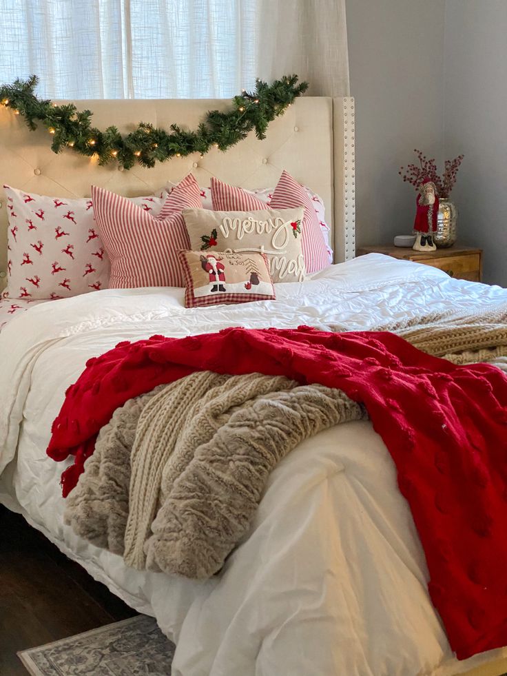 a white bed topped with pillows and blankets next to a christmas wreath on the wall