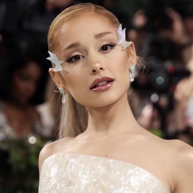 a woman with flowers in her hair and makeup looks off to the side as she stands next to a camera