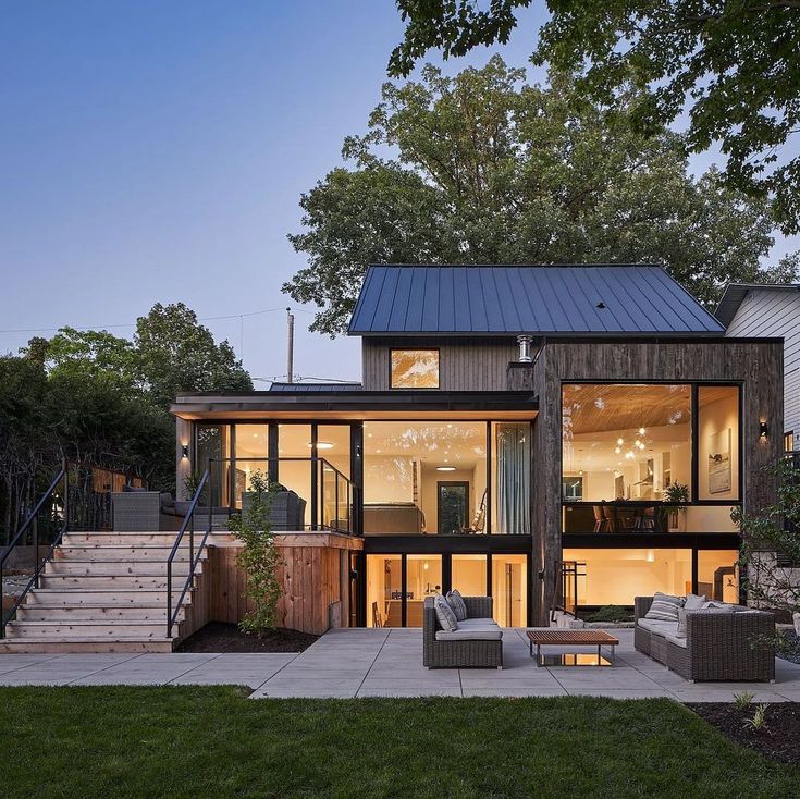 a house with glass walls and stairs leading up to the upper level, surrounded by trees