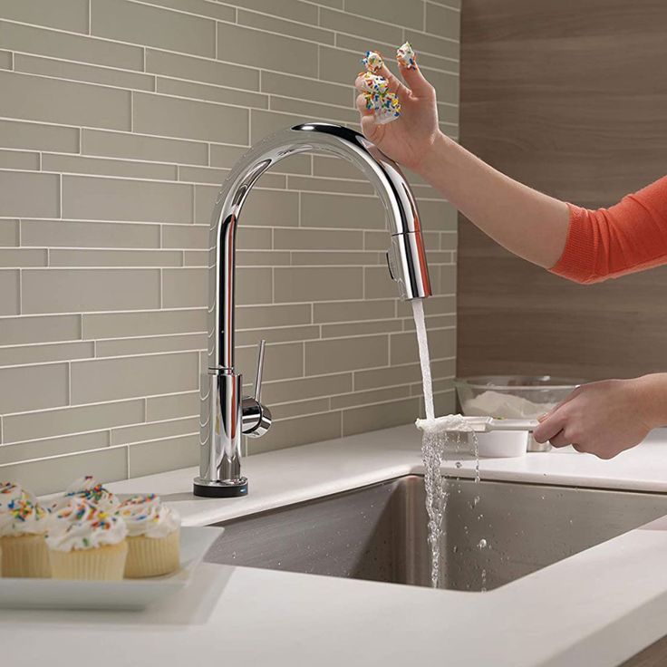 a woman washing cupcakes in a kitchen sink with a faucet running