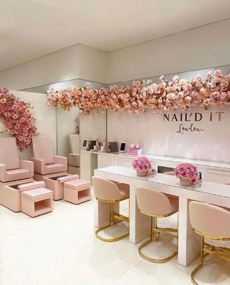 the interior of a nail salon with pink chairs and flowers hanging from the wall above it