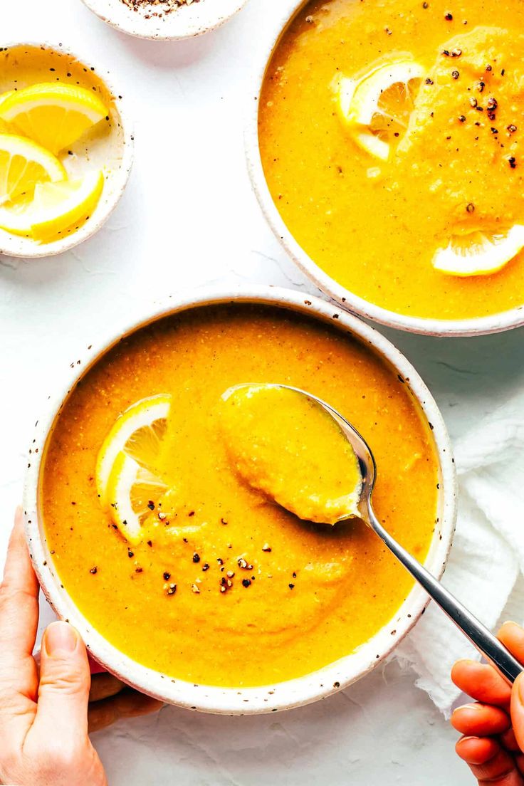 two bowls of soup with spoons in them and lemon slices on the table next to it