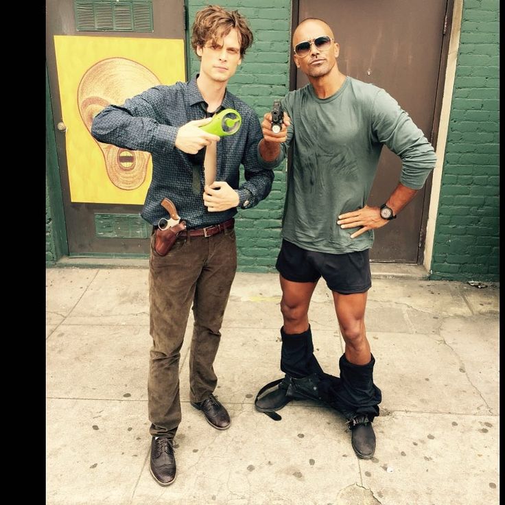 two men standing next to each other on the sidewalk with one holding a green object