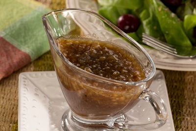 a glass gravy dish on a plate next to a salad