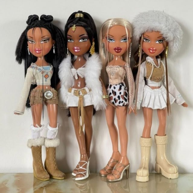 four dolls are standing next to each other in front of a white wall and one has her hair pulled back