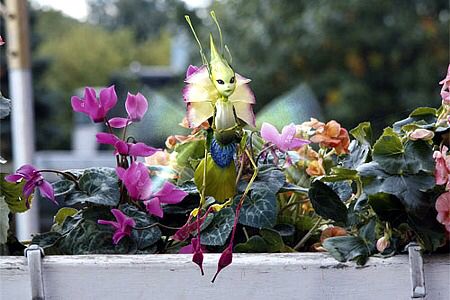 a green insect sitting on top of pink and purple flowers in a potted plant