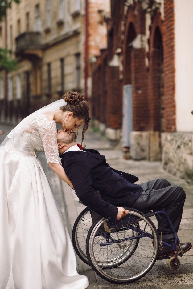 a man in a wheelchair kissing a woman's face on the cheek as they stand next to each other