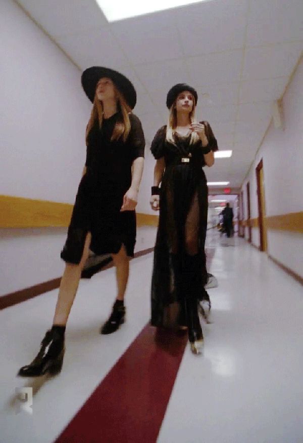 two women in black dresses and hats are walking down the hallway with their legs crossed