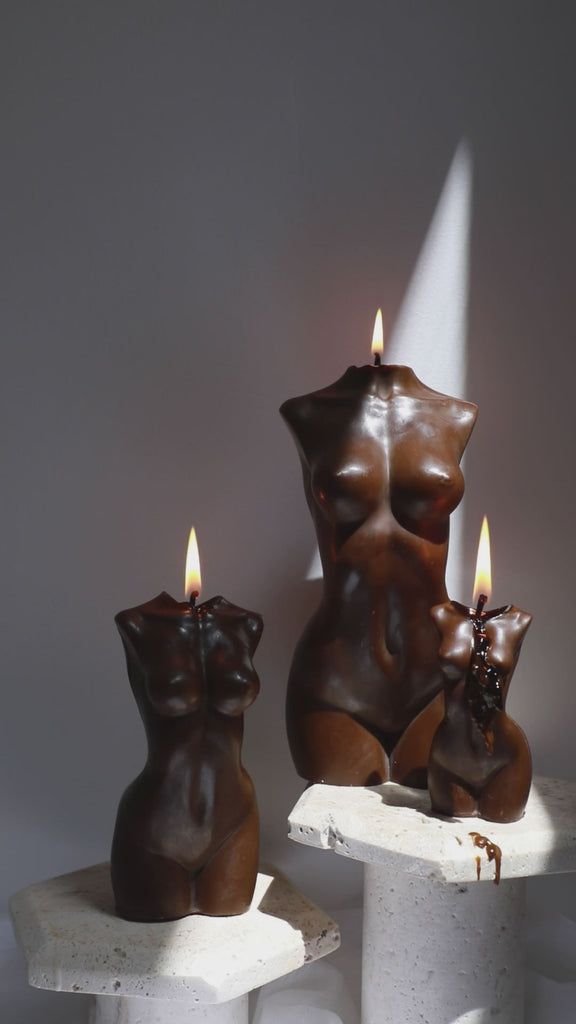 two brown candles sitting on top of each other in front of a white wall with the light coming from behind them