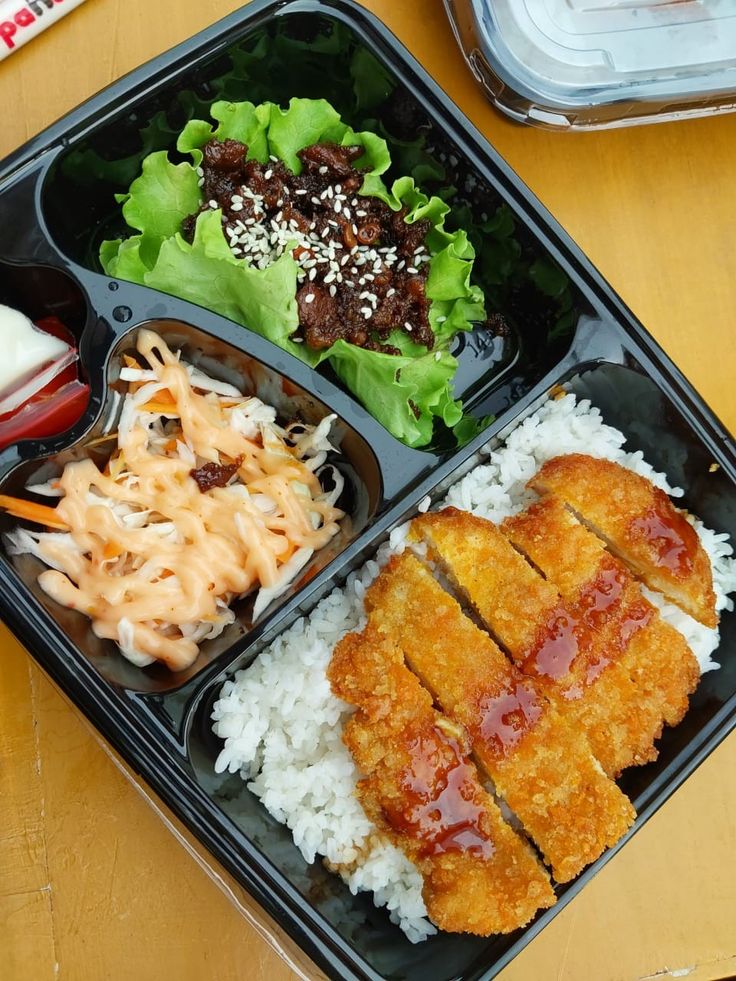 a bento box with rice, meat and vegetables on it sitting on a table