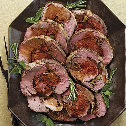 roast beef with herbs and spices on a black plate next to utensils for serving