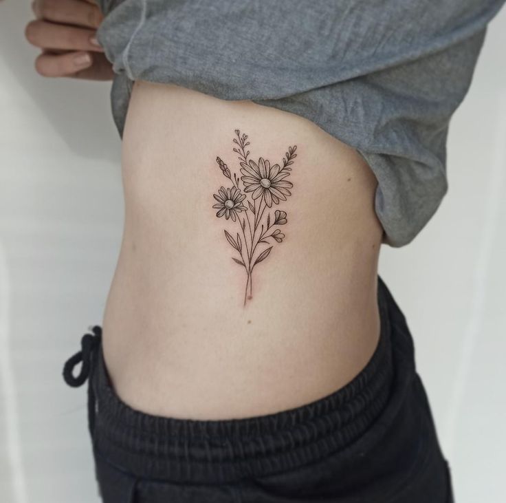 a woman's stomach with a flower tattoo on her side and the bottom part of her lower body