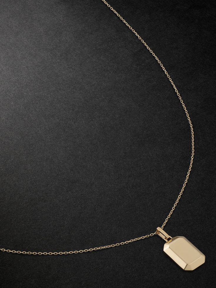 a gold plated necklace with a square pendant on it's chain, against a black background