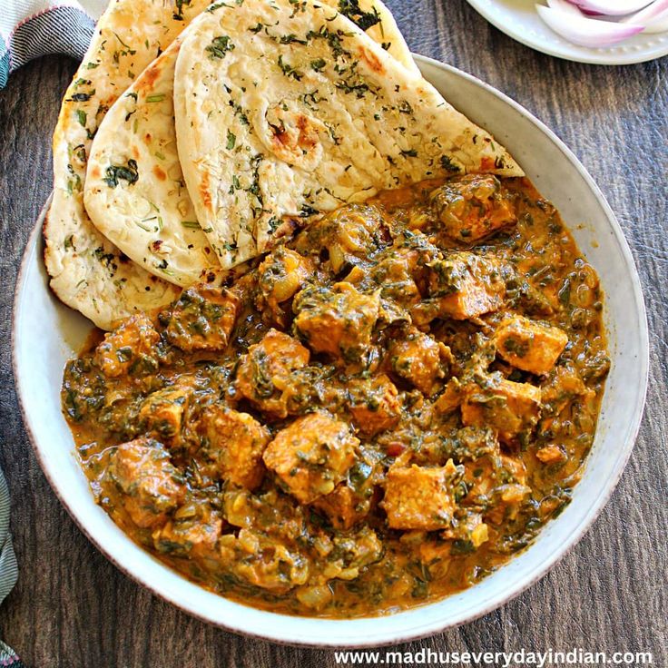 a white bowl filled with chicken curry and pita bread on top of a wooden table