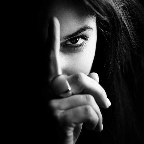 a woman making the middle finger sign with her hand in front of her face, against a black background