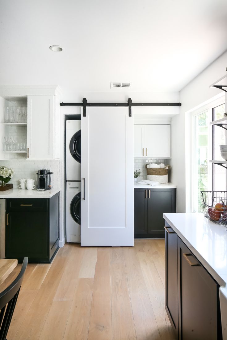 a kitchen with white cabinets and black appliances in the background is an open door leading to a washer and dryer