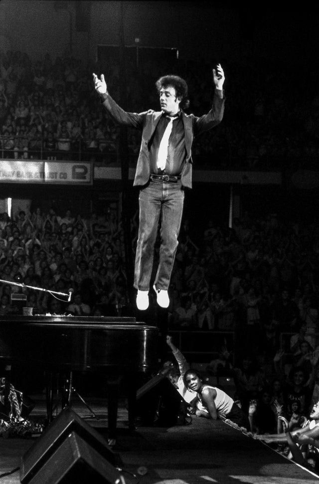 a man standing on top of a piano in front of an audience at a concert