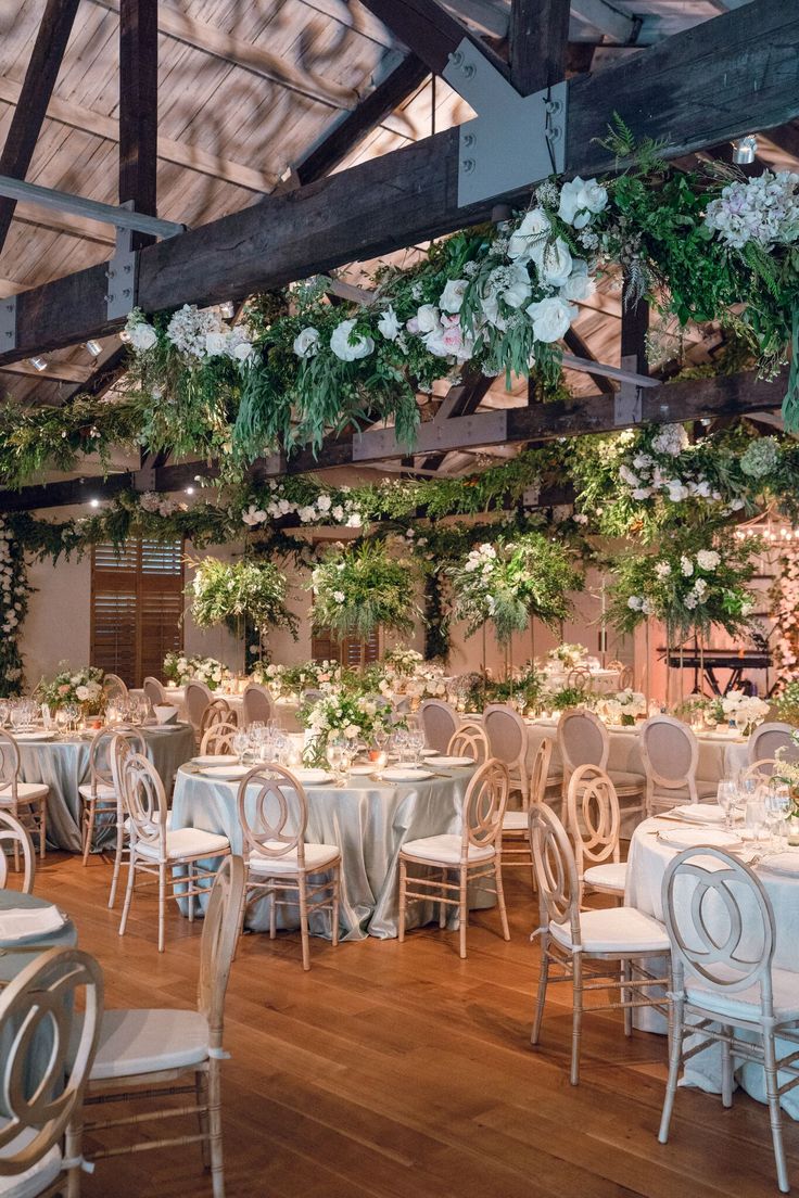 an indoor wedding venue with white linens and greenery hanging from the ceiling over tables