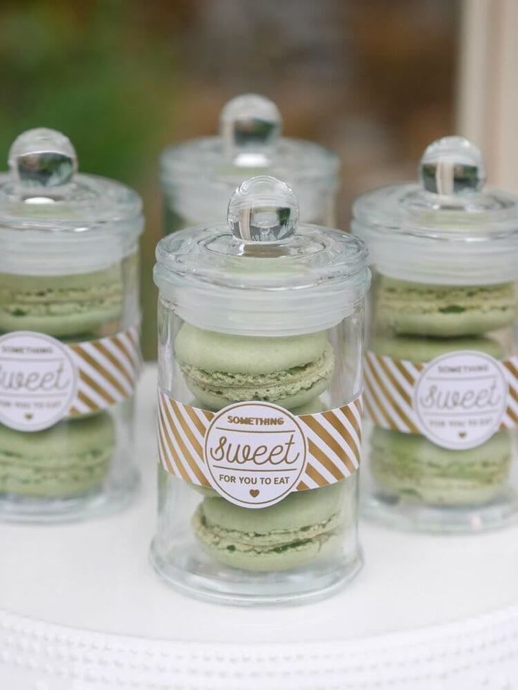 three jars filled with green macaroons sitting on top of a white cake table