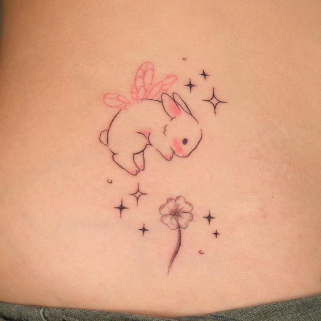 a woman's stomach with a small rabbit tattoo on the side and stars around it