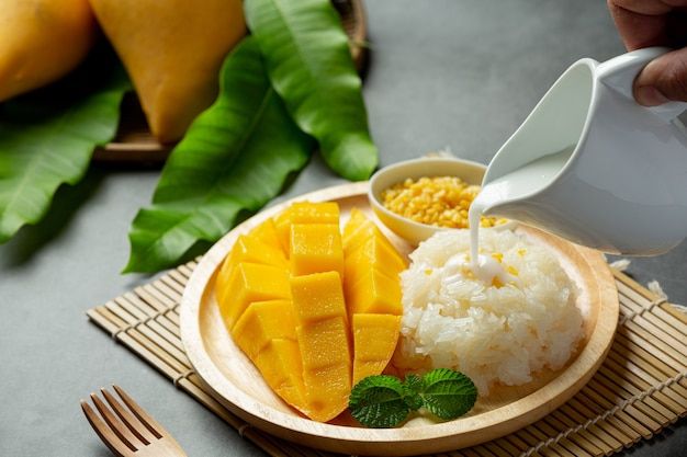 a person pours milk into a bowl filled with rice, mangoes and green leaves