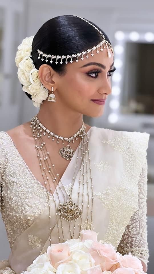 a woman in a bridal gown holding a bouquet of flowers and wearing pearls on her head