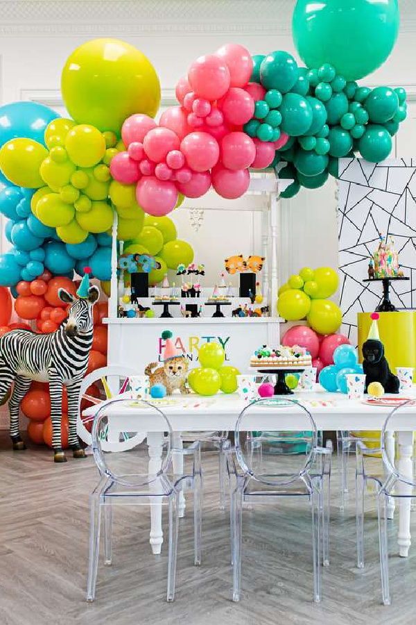 a party with balloons, giraffes and zebras on the floor in front of a table