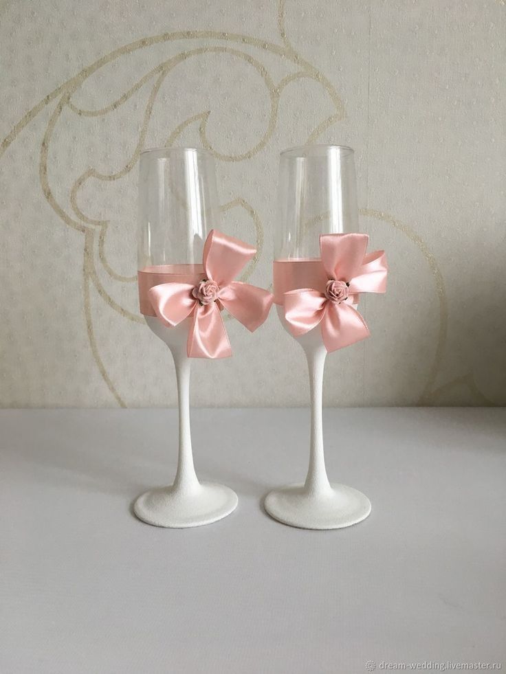 two wine glasses with pink bows on them sitting side by side in front of a wall