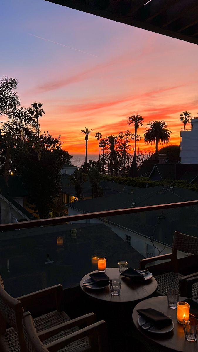 an outdoor dining area with table, chairs and candles lit up at sunset over the ocean